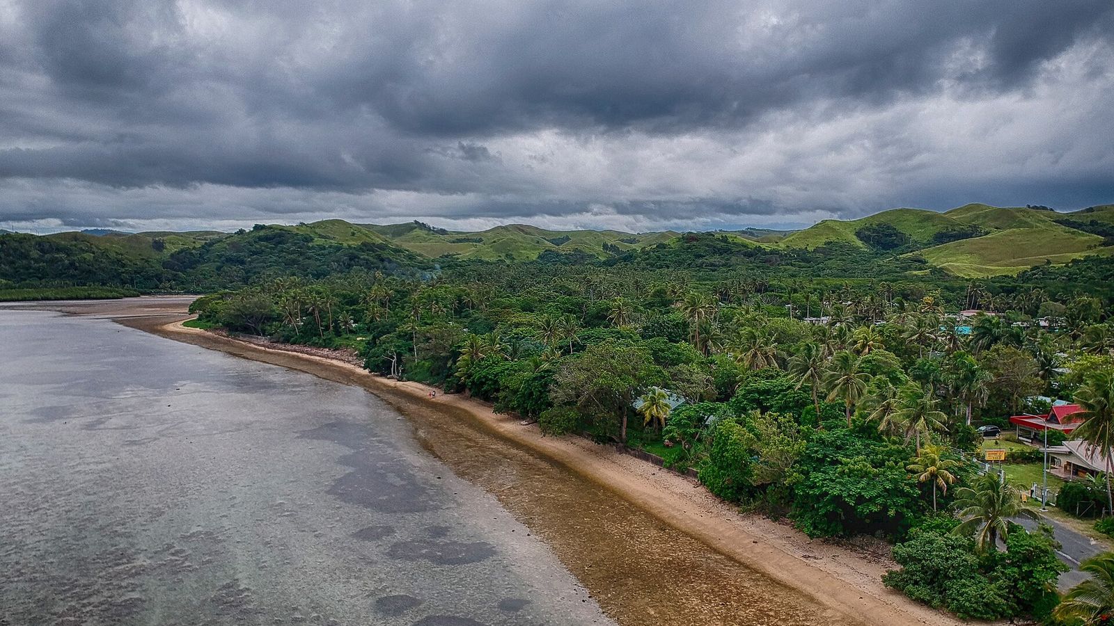 Kustlijn van de Coral Coast met een rif bij laagwater, palmen en groene heuvels