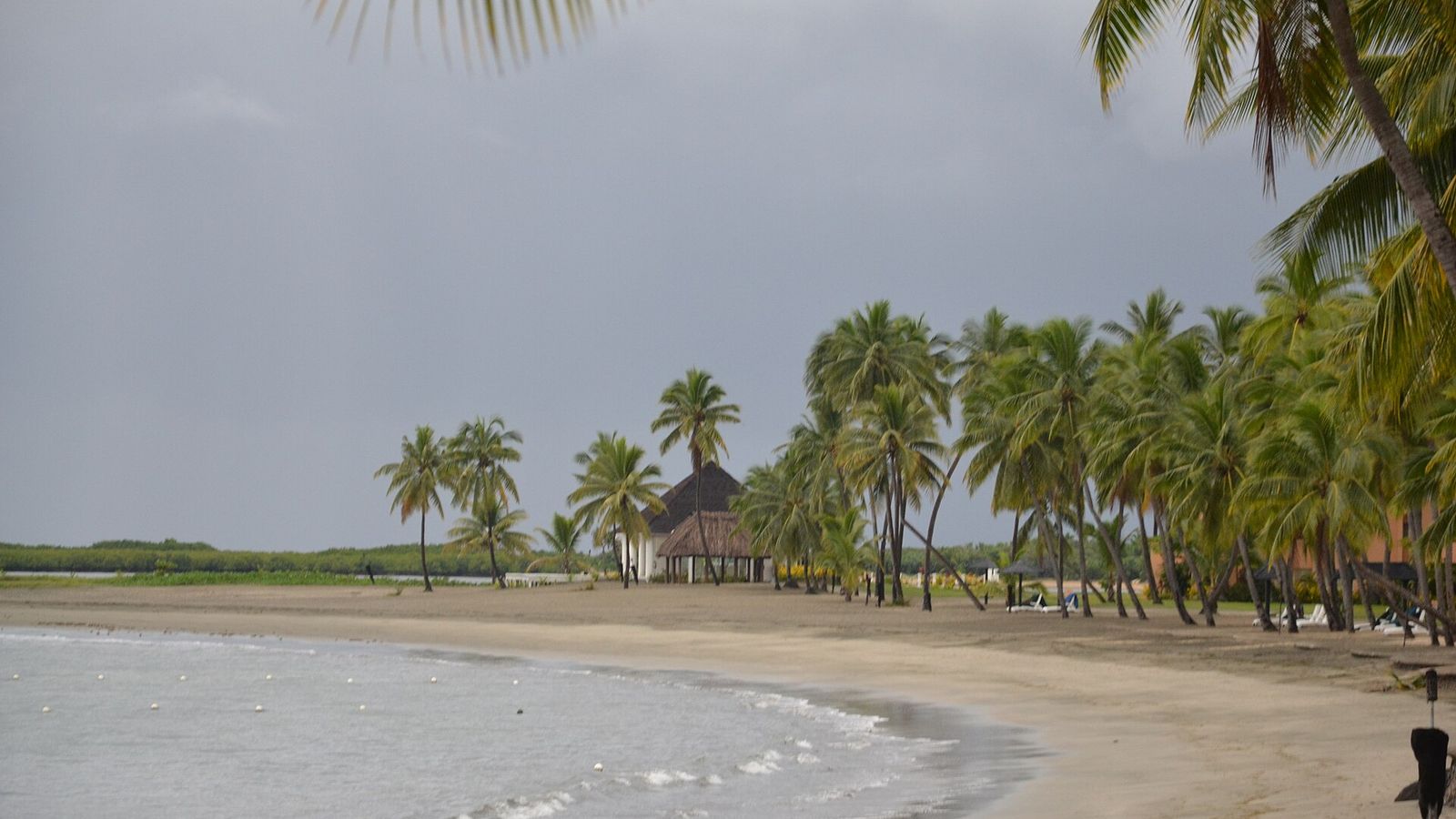 Strand van Denarau met palmbomen en een rieten paviljoen onder een grijze lucht