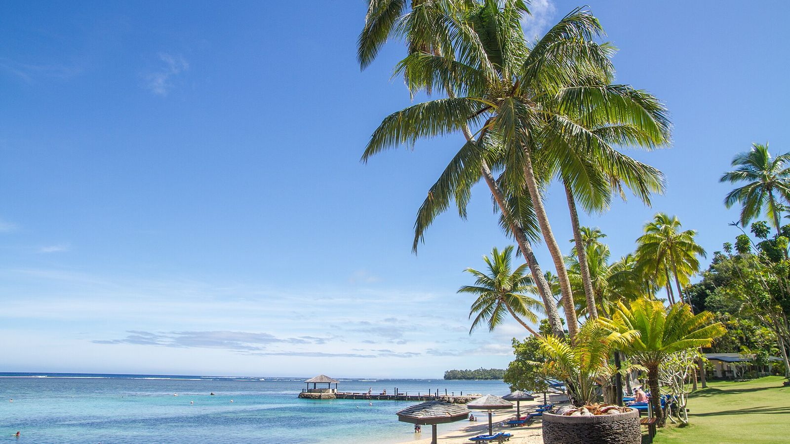 Strand met palmen, parasols en een steiger bij het Warwick Fiji Resort aan de Coral Coast