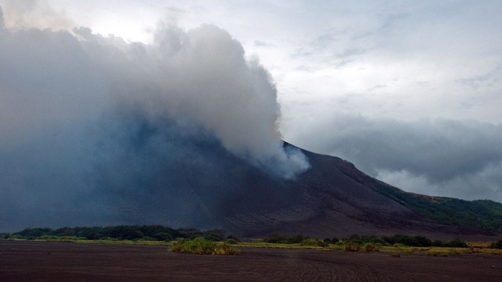 Asvlakte aan de voet van de vulkaan Mount Yasur op Tanna, Vanuatu, met een rookpluim boven de krater